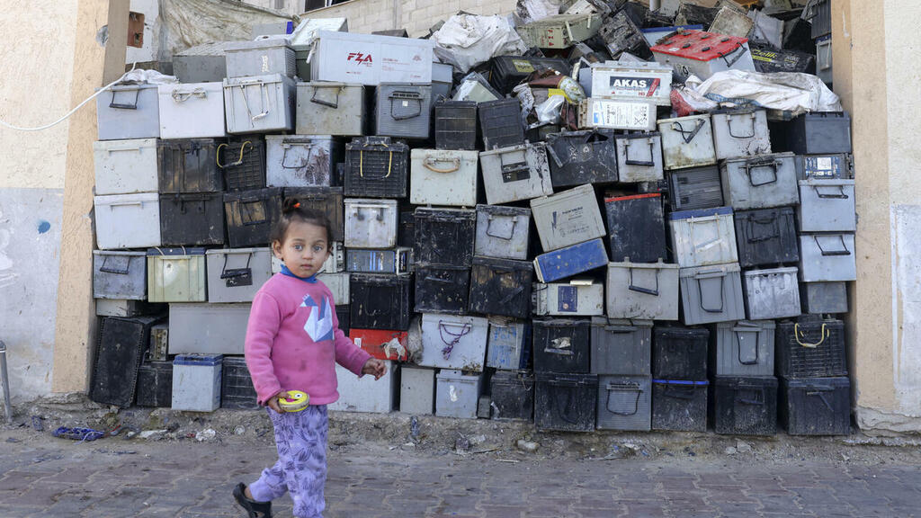 A Palestinian girl walks past a stack of discarded batteries slated for recycling in Khan Yunis