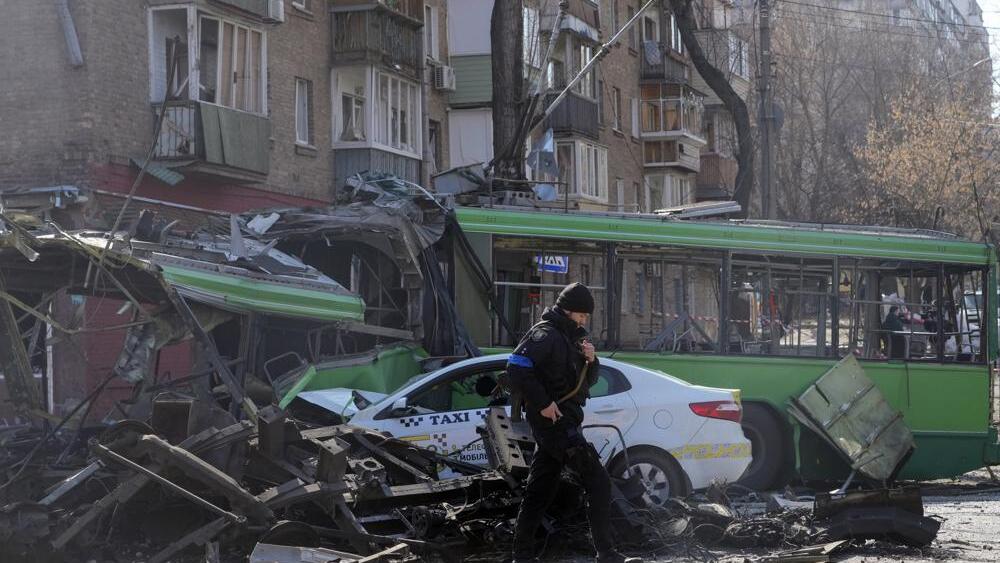 A Ukrainian soldier passes by a destroyed a trolleybus and taxi after a Russian bombing attack in Kyiv