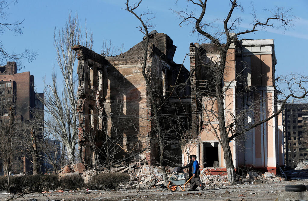 People walk by the buildings destroyed by Russian attacks in Mariupol 