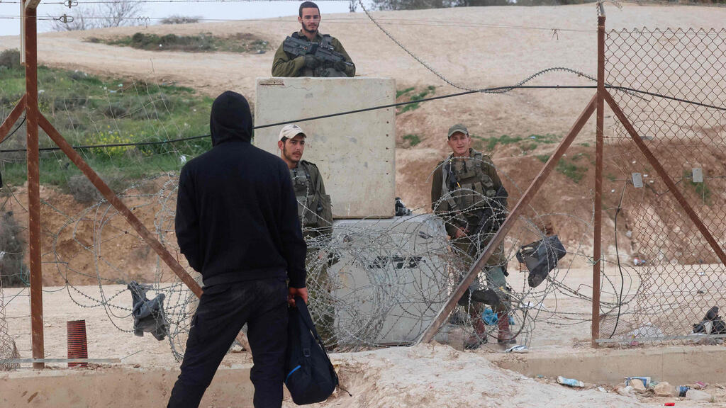 A Palestinian stands in front of a perimeter fence in the West Bank guarded by IDF troops (Photo: AFP) כוחות צה"ל ליד פרצה ב גדר ליד חברון