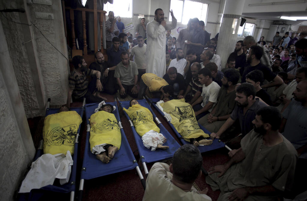 Palestinians mourn over the lifeless bodies of four boys from the same extended Bakr family, covered with yellow flags of Fatah movement, in the mosque during their funeral in Gaza City, July 16, 2014