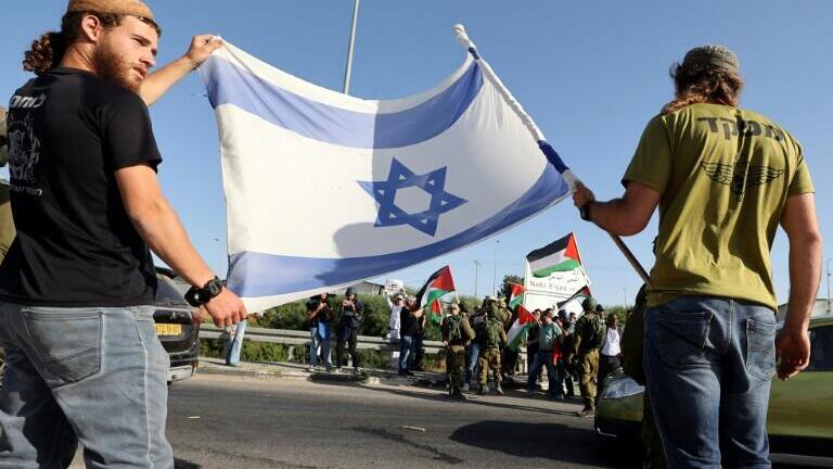 Israeli security forces stand between Jewish settlers and Palestinians, accompanied by Israeli and foreign activists, each side carrying their flags in West Bank