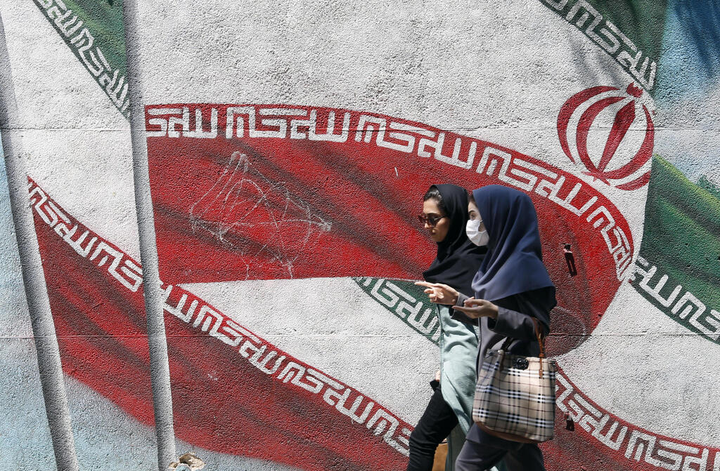 Iranian girls walk past a wall painting of Iran’s national flag in a street in downtown of Tehran