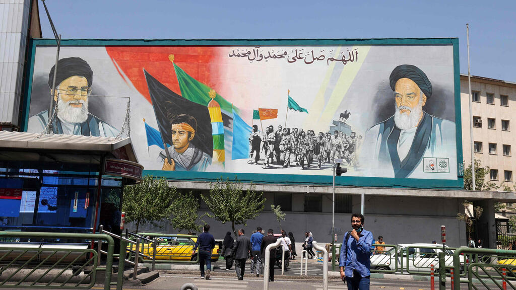 איראן איראנים הולכים בבירה טהרן ליד שלט של האייתוללות עלי חמינאי ו רוחאללה חומייני יום אחרי הניסיון לרצוח את סלמן רושדי