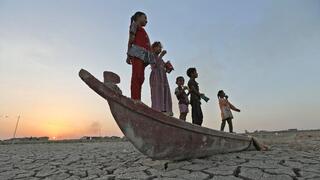 ילדים עומדים על סירה המונחת על המצע היבש של ביצות צ'יבאייש בעיראק