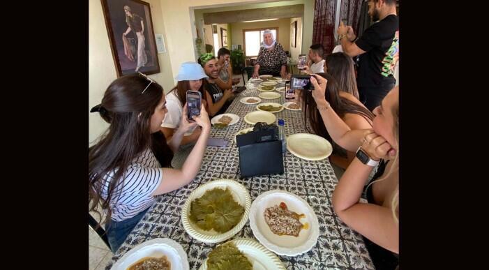 Participants of the influencers’ tour direct their phones at Maha Amer, a Druze cook known as “Savta Maha” (Grandma Maha) as she teaches them the art of making stuffed vine leaves 