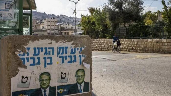 A man cycles near a concrete block bearing posters depicting far-right Israeli MK Itamar Ben Gvir, in the West Bank city of Hebron 