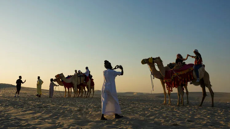 A tour guide takes a photo of a couple atop camels in Mesaieed, Qatar 