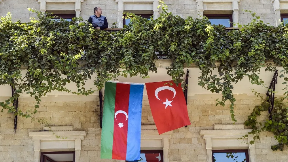 A man stands on the balcony of a hotel with its facade decorated with flags of Azerbaijan and Turkey in the Old Town of Baku, Azerbaijan (Photo: TOFIK BABAYEV / AFP) man stands on the balcony of a hotel with its facade decorated with flags of Azerbaijan and Turkey in the Old Town of Baku, Azerbaijan