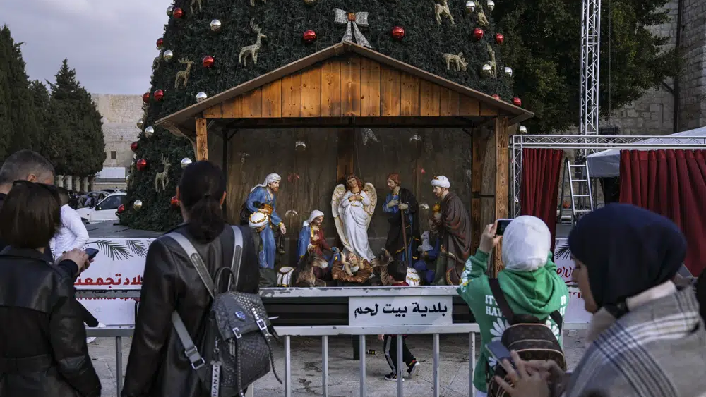 People take pictures of the Christmas tree and nativity scene in Manger Square, outside to the Church of the Nativity, traditionally believed by Christians to be the birthplace of Jesus Christ, ahead of Christmas, in the West Bank city of Bethlehem, Monday, Dec. 5, 2022