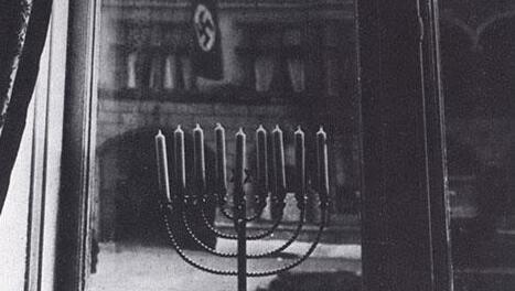 A photograph taken in 1931, by Rachel Posner, shows the candle-lit Hanukkah menorah against the backdrop of the Nazi flags on a building across the street for their home