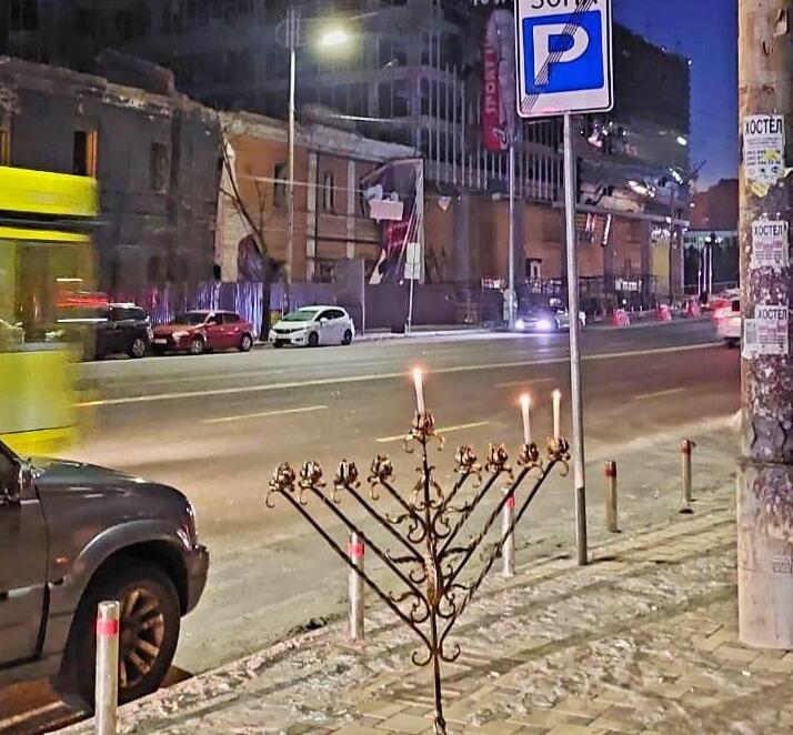 A lit menorah in front of buildings damaged by Russian shellings in Kyiv (Photo: Beit Menachem JCC) אור החנוכה הודלק על רקע הבניין המופגז של חברת האנרגיה בקייב