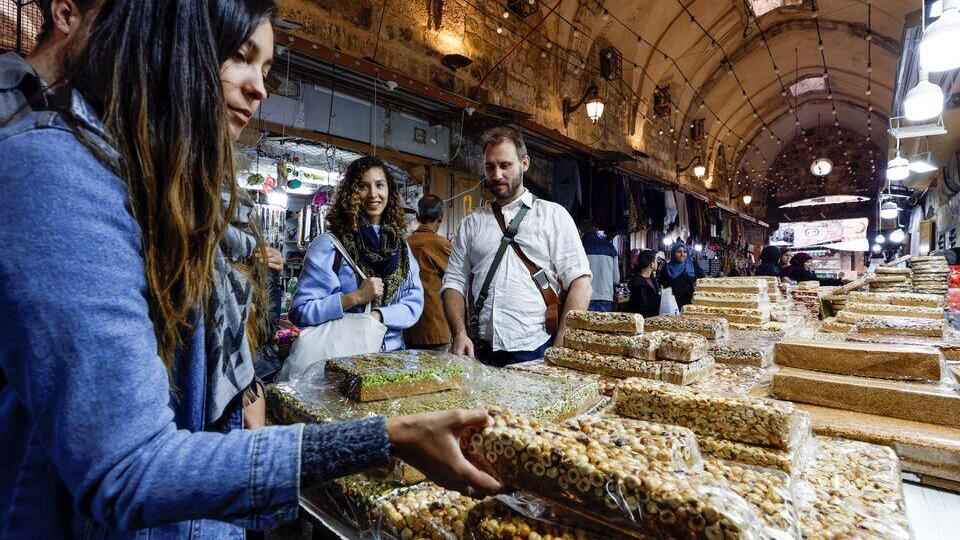 Tourists browse at a sweet dessert stall in a market, Jerusalem's Old City, December 11, 2022 