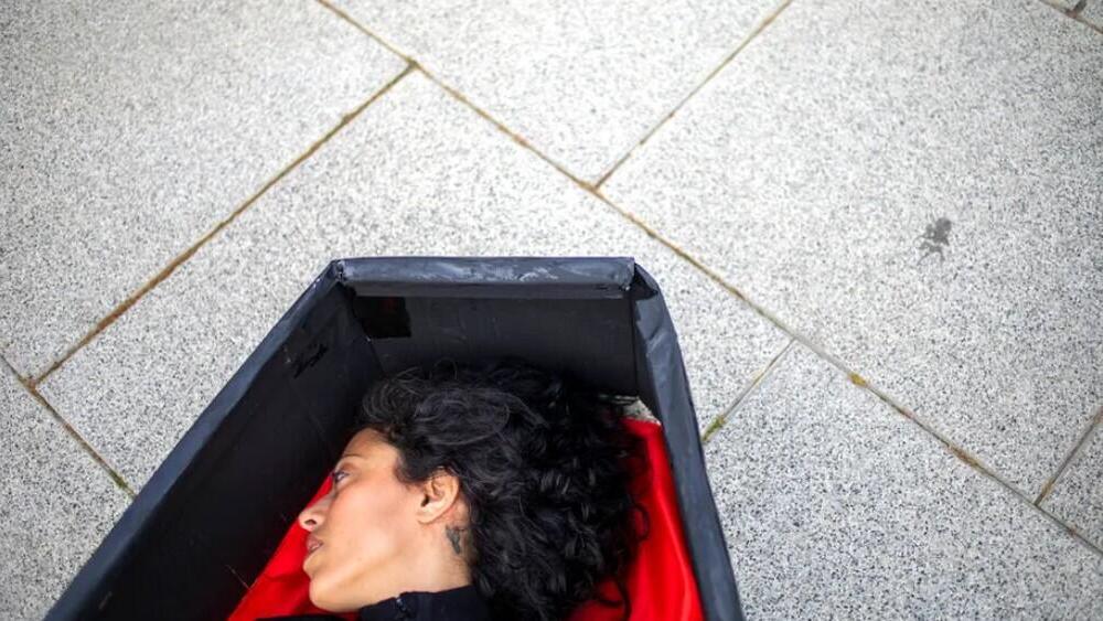 A woman lays in a coffin representing women killed in domestic violence in front of Tel Aviv 