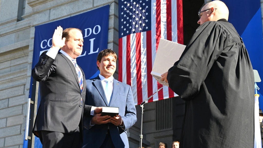 Brian Boatright, the chief justice of the Colorado Supreme Court, at right, swears in Gov. Jared Polis, on the left, while Polis's husband, Marlon Reis, holds a Hebrew bible, in Denver, Jan. 10, 2023 