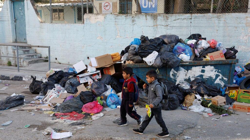 Palestinian kids pass a pile of garbage in Al Jalazone refugee camp near Ramallah, in the Israeli-occupied West Bank, January 25, 2023 