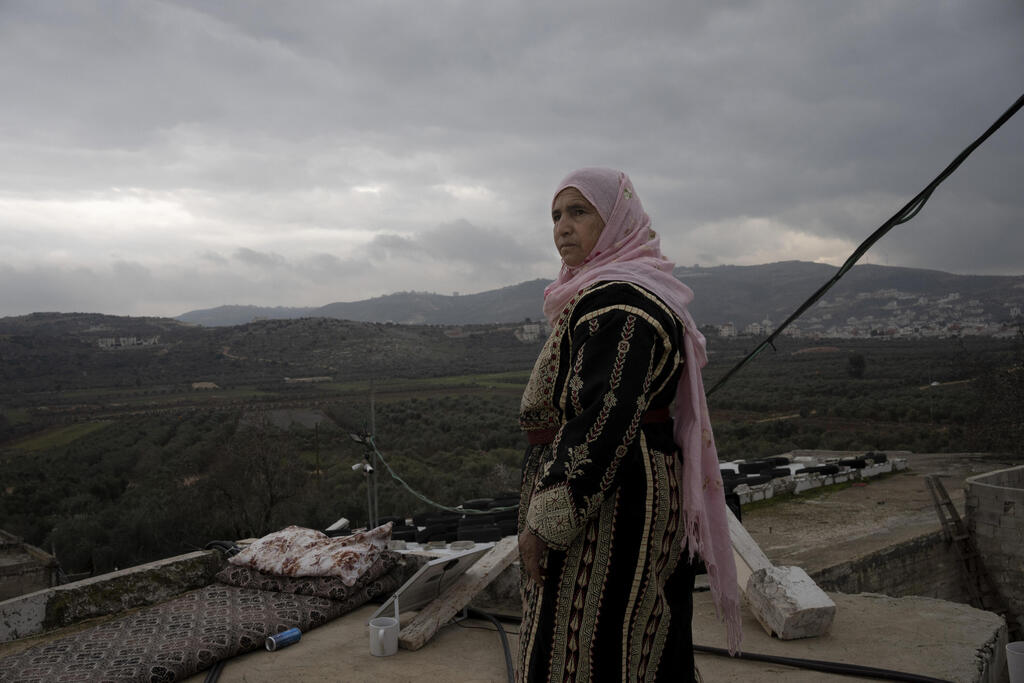 Amal Abu Awad, mother of nine, stands on her roof beside a sleeping mat used by a family member on an overnight guard shift, in the West Bank town of Turmus Aya 