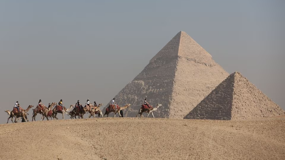 Tourists ride camels in front of the Great Pyramids plateau in Giza, Egypt December 11, 2022 