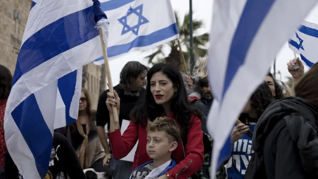 A woman waves an Israeli flag at a demonstration in solidarity with Palestinians as part of ongoing protests against plans by Israeli Prime Minister Benjamin Netanyahu's government to overhaul the judicial system, in Jaffa, Israel, Thursday, March 23, 2023 