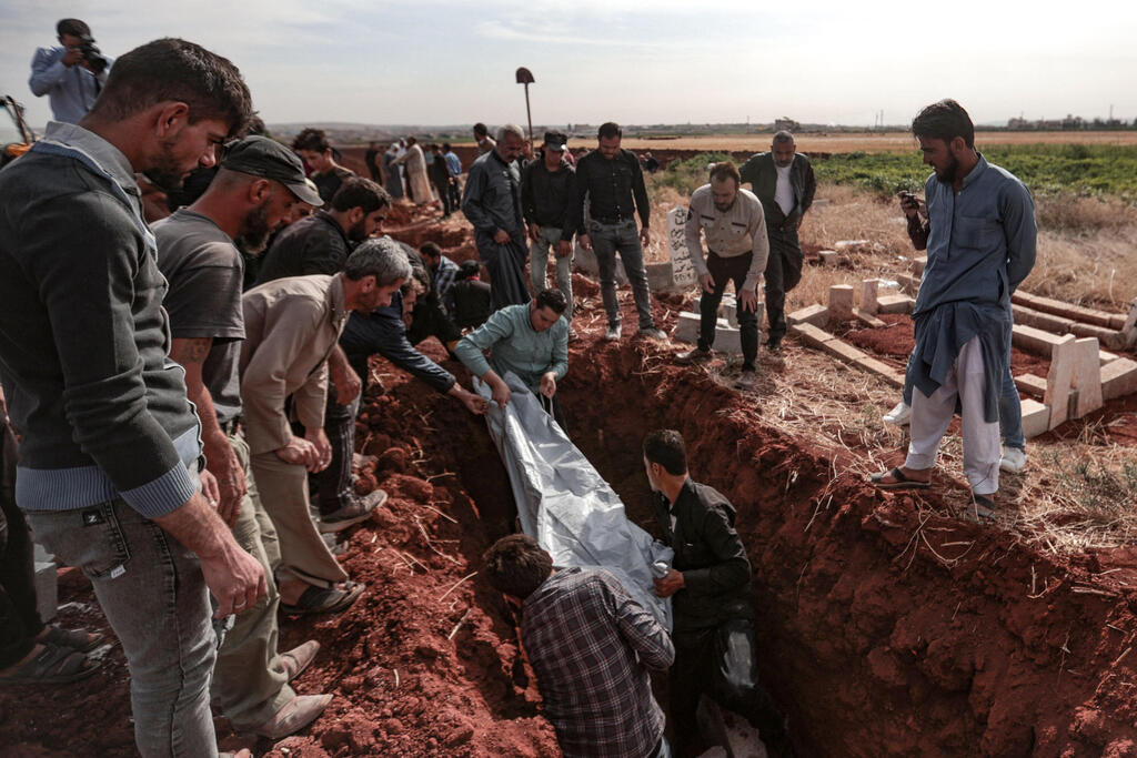 people watch the burial of the bodies of an elderly woman and four of her children killed during an overnight bombardment by Syrian regime forces 