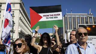 מפגינה באתונה אוחזת שלט שעליו נכתב "מהנהר לים"