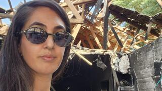 דורין כהן על רקע ביתה השרוף בכפר עזה