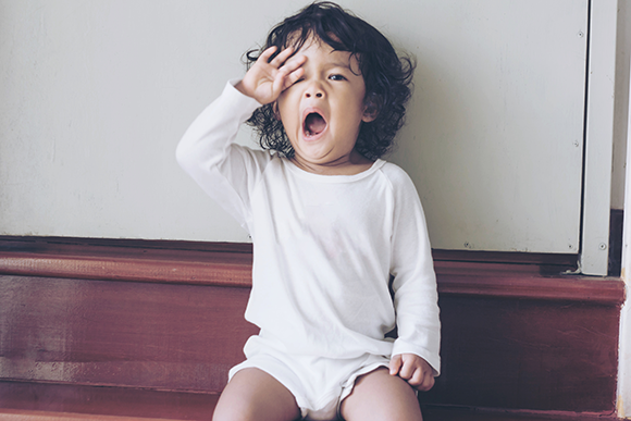 Yawning is an involuntary physical act. A toddler rubs her eyes and yawns 