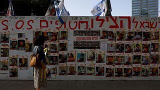 אישה מביטה על תמונות החטופים בעזה על קיר בתל אביב