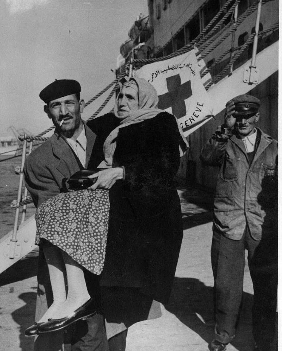 פליט יהודי ממצרים נושא את אימו הקשישה בירידה מהסיפון בנמל פיראוס, 1957