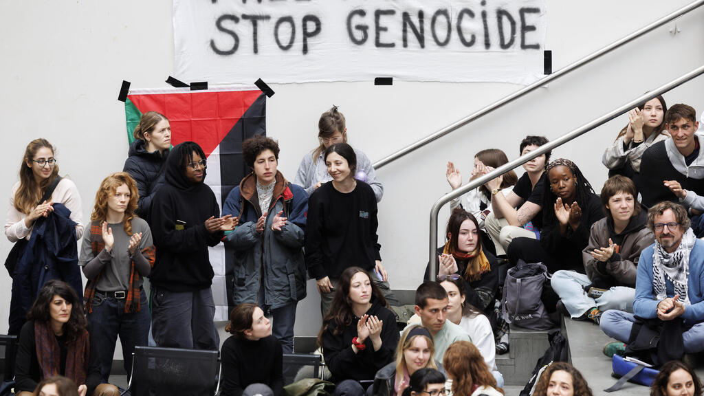 סטודנטים פרו-פלסטינים בז'נבה, שווייץ, לצד שלט שקורא "לשחרר את פלסטין" ומאשים את ישראל ב"רצח עם"