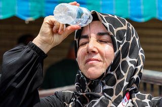Turkish Muslim pilgrim pours cold water from a bottle on her head to cool off