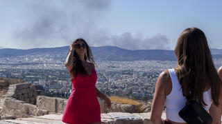 תיירת מצטלמת באקרופוליס כשמאחוריה ברקע עשן של שריפות