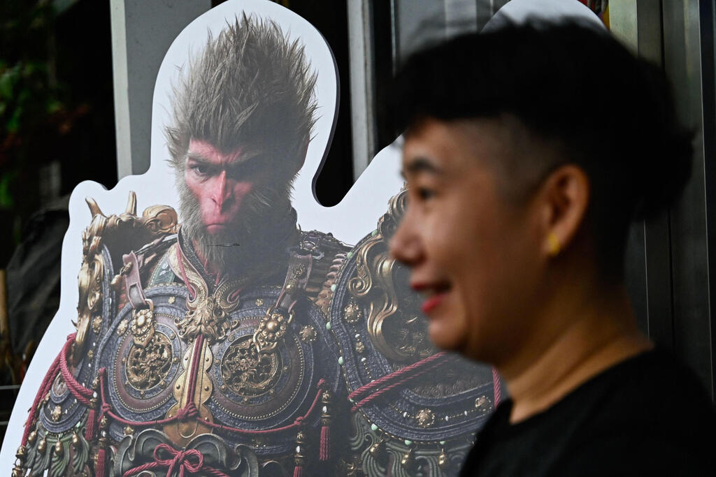 A woman stands next to a cardboard cutout of the 'Monkey King' character, or 'Sun Wukong', of the Chinese action role-playing game 'Black Myth: Wukong' during its launch day in Beijing