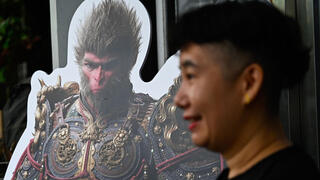 A woman stands next to a cardboard cutout of the 'Monkey King' character, or 'Sun Wukong', of the Chinese action role-playing game 'Black Myth: Wukong' during its launch day in Beijing