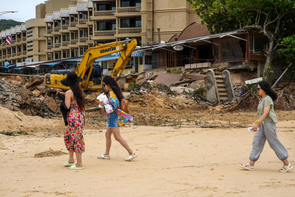 Tourists walk past a tractor used to clear an area after thirteen people, including a Russian couple, died in a mudslide on the Thai resort island of Phuket, Thailand, August 25, 2024 