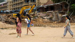 Tourists walk past a tractor used to clear an area after thirteen people, including a Russian couple, died in a mudslide on the Thai resort island of Phuket, Thailand, August 25, 2024 