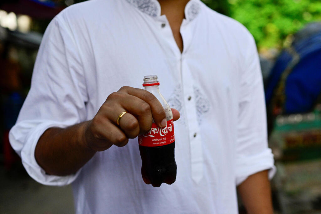 A man holds a Coca-Cola soft drink along a street in Dhaka, Bangladesh