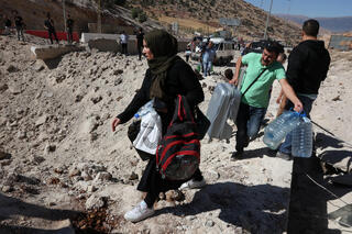People carry belongings across the Masnaa Lebanon-Syria border after an Israeli strike 