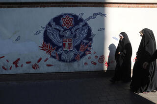 Iranian women pass in front of an anti-U.S. mural on a street in Tehran