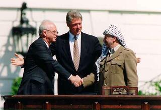 Prime Minister Yitzhak Rabin shakes hands with PLO Chairman Yasser Arafat as President Bill Clinton looks on at the White House after the signing of the Oslo Accords in 1993 
