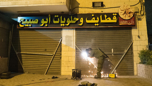 An IDF soldier working on welding shut the entance to the terrorist's family's sweet shop (Photo: IDF Spokesperson's Unit)