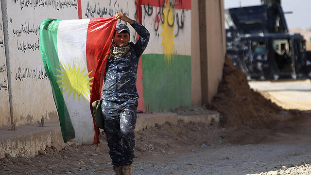 A member of the Iraqi forces holds up a Kurdish flag (צילום: AFP) A member of the Iraqi forces holds up a Kurdish flag