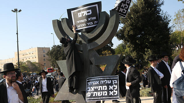 Haredi protesters near the Knesset, hanging a sign saying, "We'll happily fill the prisons"