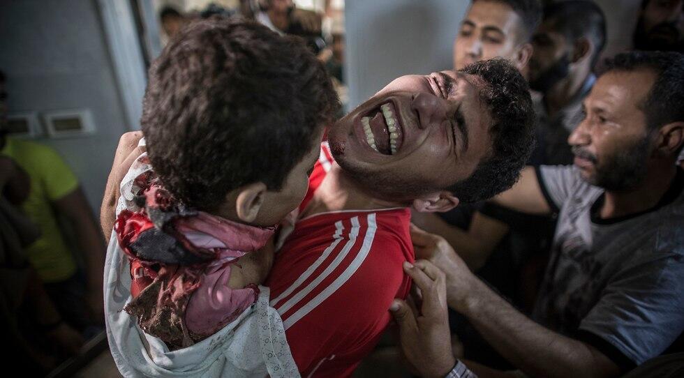 Palestinian man cries as he holds the dead body of his young brother shortly after he got killed by an Israeli naval bombardment in the port of Gaza City