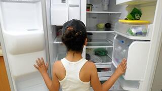 ילדה ניצבת מול מקרר כמעט ריק