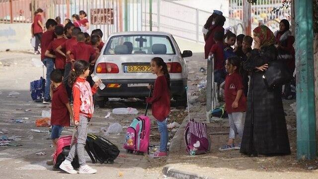 A woman and schoolchildren stand near a street in Rahat