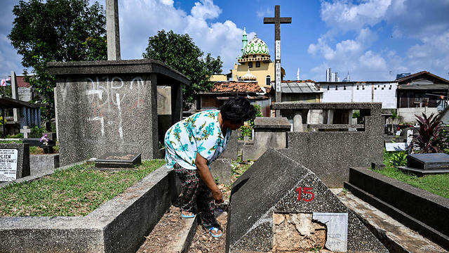 An Indonesian woman cleaning one of the Jewish tombs at a Christian cemetery in a Muslim majority neighborhood in Jakarta