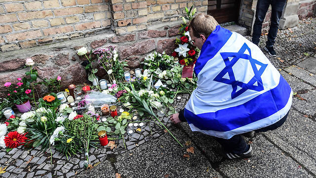 A man wrapped in an Israeli flag lays flowers at the site of the shooting (צילום: EPA) A man wrapped in an Israeli flag lays flowers at the site of the shooting