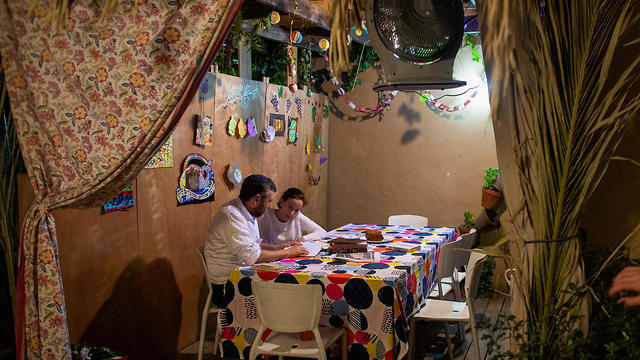Yoni Stanleigh and his daughter Nehora sit in their sukka