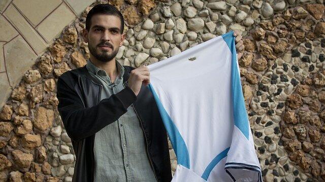 Qawasmi holds up the shirt he was wearing when he was shot